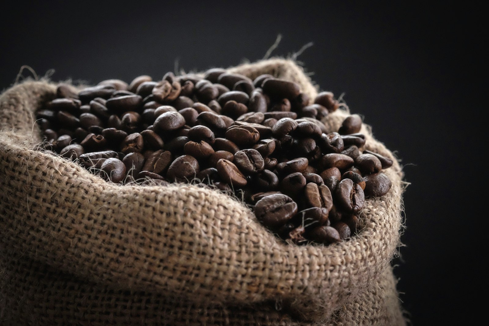 Roasted coffee beans spilling from a burlap sack against a dark background