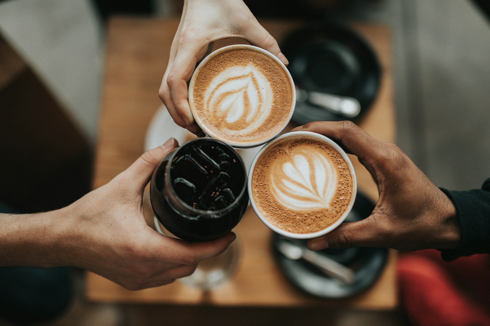 Three hands toasting with coffee cups and an iced drink