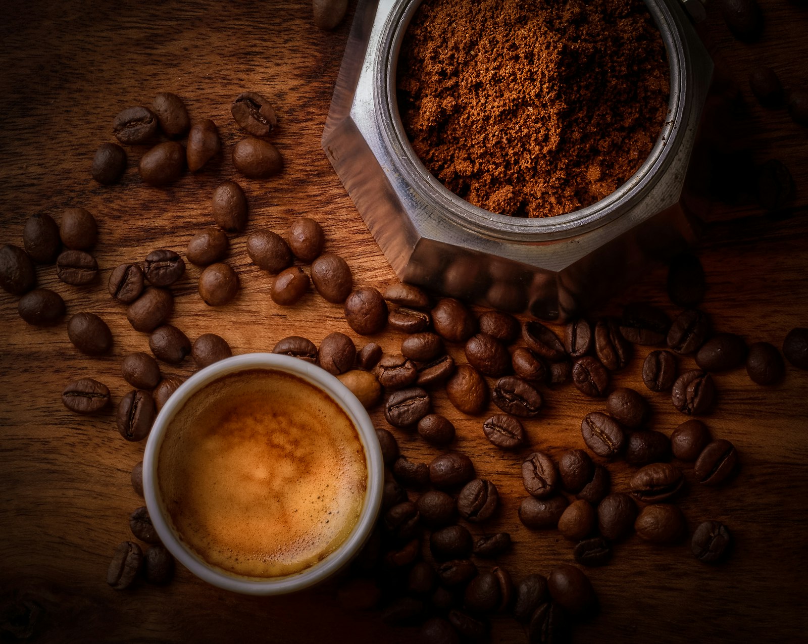 Overhead flat lay of an espresso cup, coffee beans and a grinder on dark wood