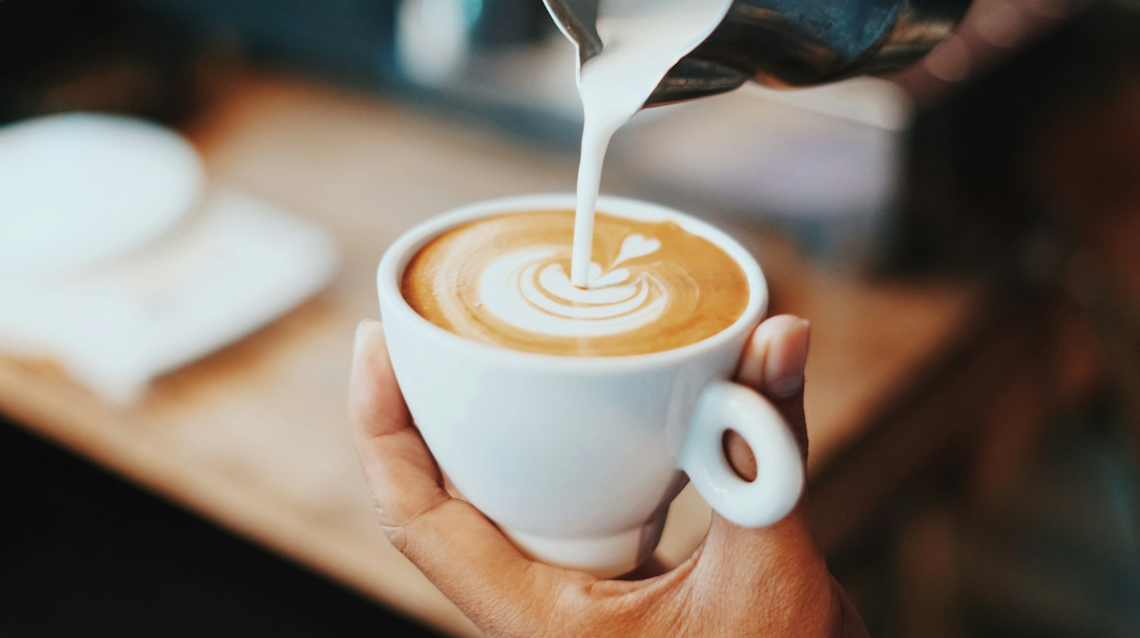White cup with heart-shaped latte art on a blue saucer