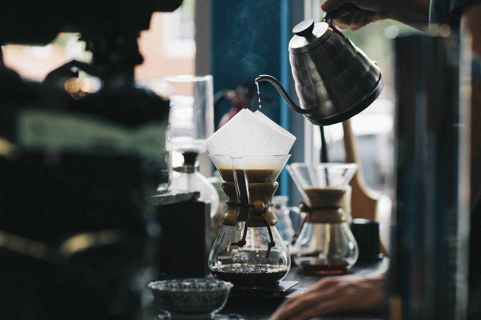 Gooseneck kettle pouring water over coffee grounds in a pour-over brewer, steam rising
