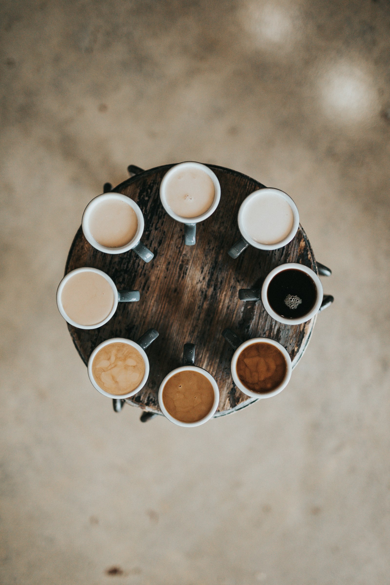 Overhead view of eight different coffee drinks arranged in a circle on a wooden table