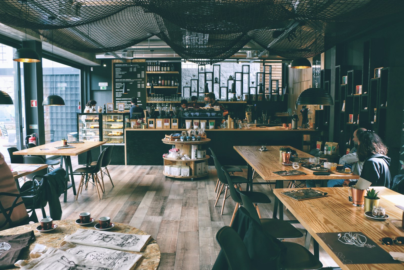 Sunlit modern coffee shop interior with wooden communal tables and large windows